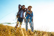 © Cookie Studio - Young couple of travelers with backpacks smiling, standing in field.