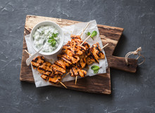 Grilled Teriyaki Chicken Skewers And Tzatziki Sauce On A Wooden Board On A Dark Background, Top View. Delicious Appetizers