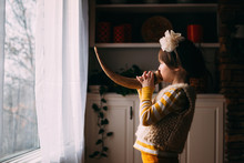 Side View Of Girl Playing With Horn In Front Of Window