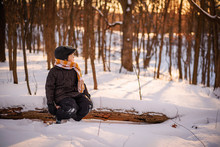 Boy Sitting On A Log In The Woods In Winter