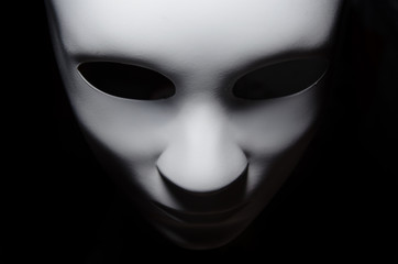 white mask with neutral expression and shadows on dark background