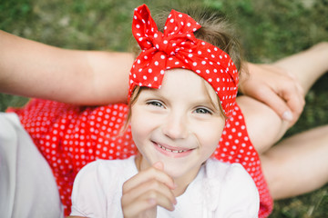 Wall Mural - Charming little girl with large red bow on her head lies on mother's knees