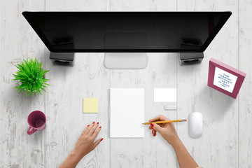 Woman write something on pad. Blank paper to add text, drawing, sketch. Computer display with blank screen beside. Blank business card and note paper beside. Top view,