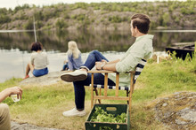 Men Having Drink While Looking At Female Friends Fishing On Lakeshore