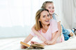 © LIGHTFIELD STUDIOS - Happy mother and daughter hugging while lying on carpet and reading book