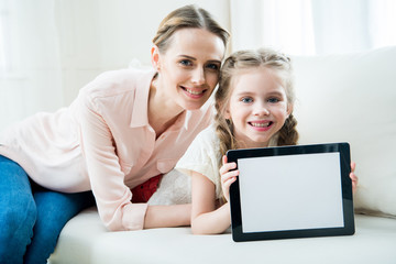 portrait of smiling mother and daughter showing digital tablet