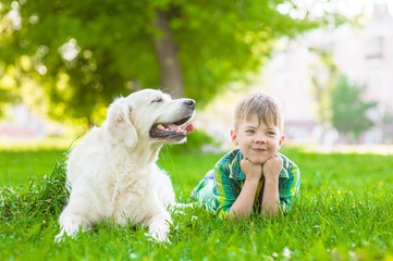 Young boy lying with golden retriever dog on green grass