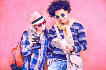 Interracial couple of tourists holding camera and looking tour guide - Attractive latinos traveler leaning at colorful city wall pointing map book smiling in happy attitude