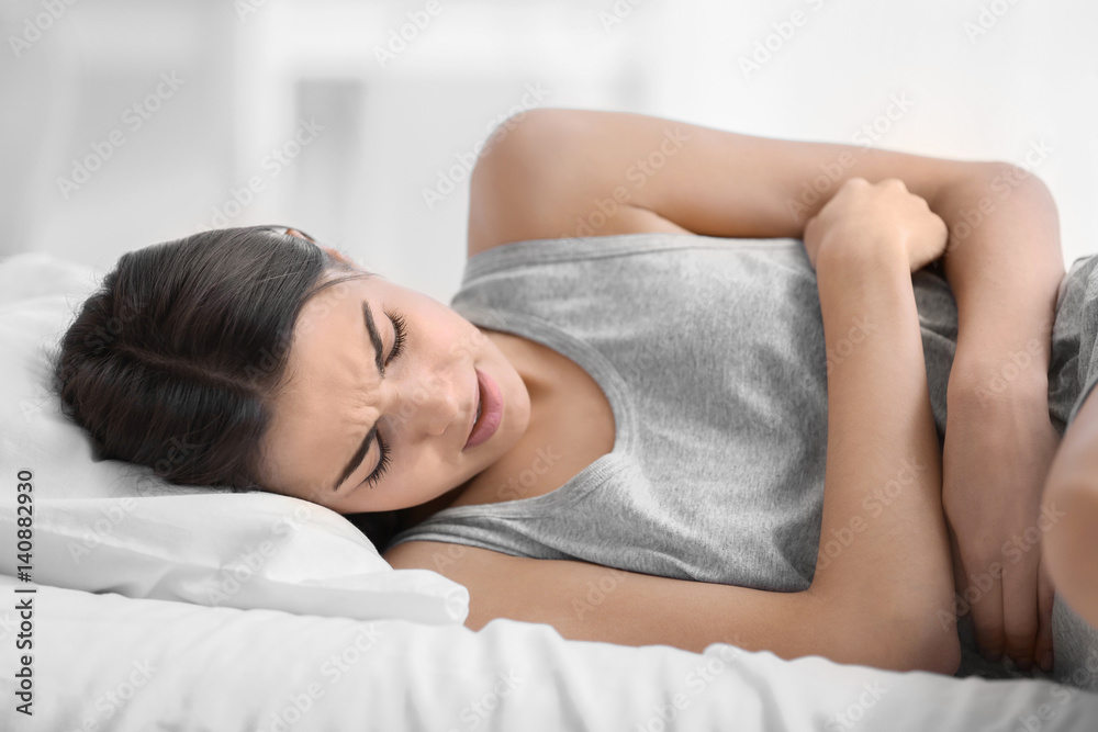 Young woman suffering from abdominal pain while lying on bed at home. Gynecology concept