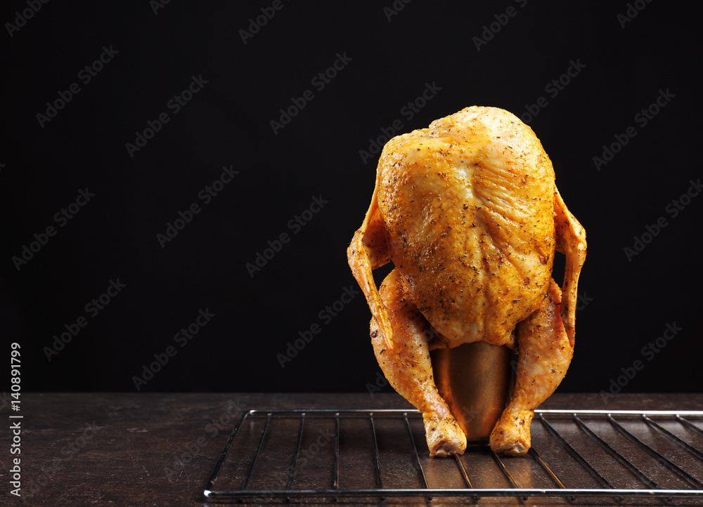 Marinaded chicken on beer can against black background