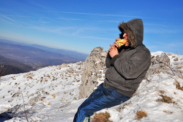 Lonely mountaineer get rest and eat sandwich on snowy mountain high above the clouds