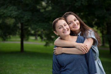 mother and adult daughter hugging and having fun together in the park outdoor in summer. portrait of
