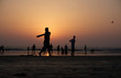 Silhouettes of locals playing beach cricket at sunset in India