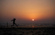 Young man playing cricket with bat on beach at sunset