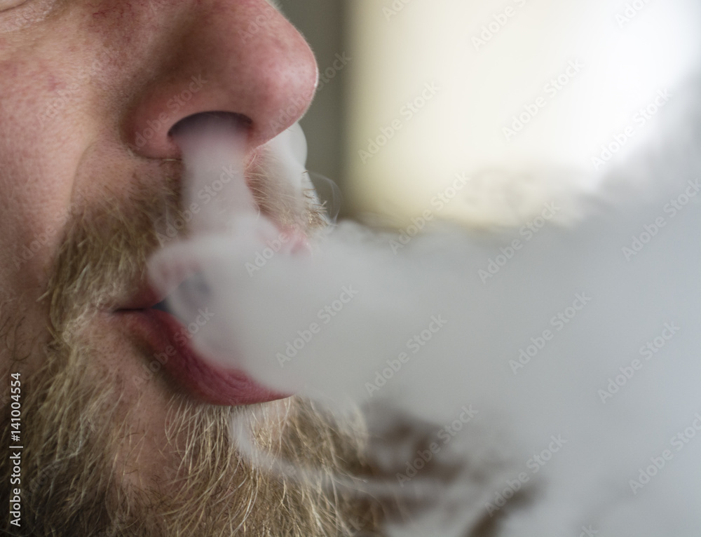 Man with beard and goatee deleted from cigarette smoke through the nose and  mouth. Stock Photo