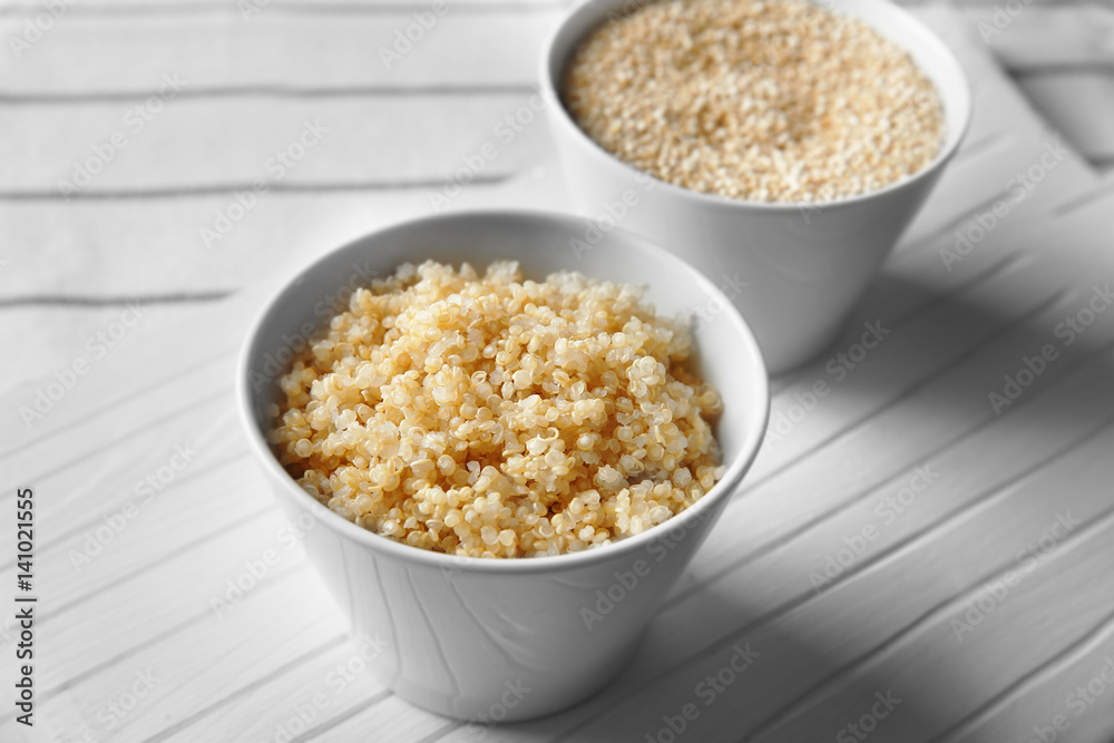 Two white bowls with sprouted organic quinoa grains on white wooden board