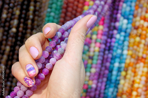 Fotografering Woman hand with manicure against of differnet colors beads