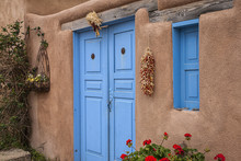 Blue Doors Of An Old Adobe House In Taos, New Mexico. Hanging Peppers And Indian Corn.