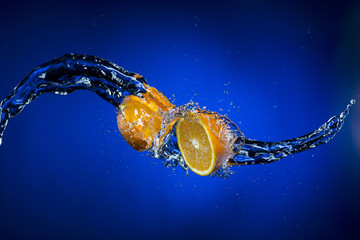 two halves of orange and splash of water on blue background