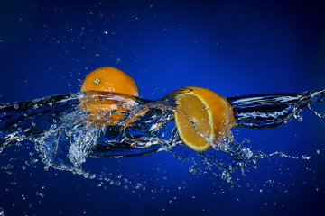 two halves of orange and splash of water on blue background