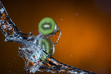 two halves of kiwi and splash of water on orange background