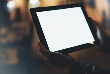 Girl holding in hands on blank screen tablet on background illumination glow bokeh light in night atmospheric city, hands using template mobile computer on lights glitter street; mock up gadget