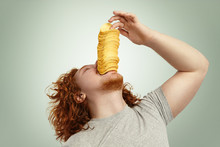 Indoor Shot Of Overweight Young Bearded Male With Red Curly Hair Throwing Head Back, Performing Trick, About To Eat Pile Of Potato Chips At A Time. People, Unhealthy Lifestyle, Diet And Obesity
