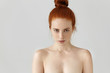 People, youth and beauty. Isolated portrait of attractive young Caucasian female with ginger hair knot posing topless indoors, having freckles all over her face and shoulders, staring at camera
