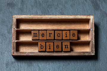 Wall Mural - Mercie bien. Thank you very much written in French translation. Vintage box, wooden cubes phrase with old style letters. Gray stone textured background. Close-up, up view, soft focus