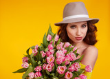 Fototapeta Tulipany - Beautiful girl with flowers tulips in hands on a light yellow background