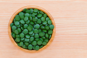 green pills spirulina and chlorella seaweed close up in a wooden bowl top view