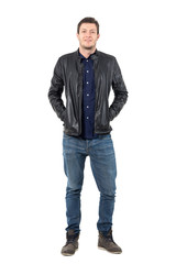 Wall Mural - Relaxed man in jeans and leather jacket smiling at camera with hands in pockets. Full body length portrait isolated over white studio background. 