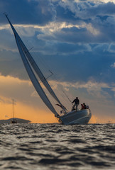 Wall Mural - Sailing boat with crew on board during sunset