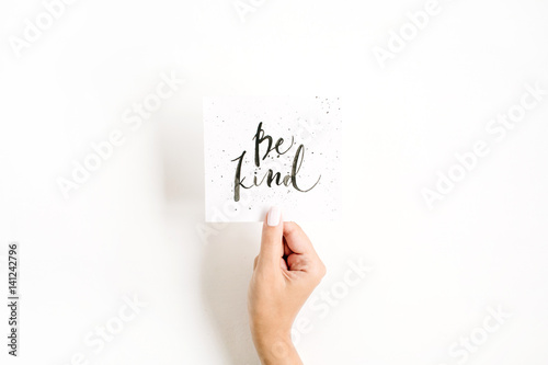 Photographie Minimal pale composition with girl's hand holding card with quote Be Kind written in calligraphic style on paper on white background