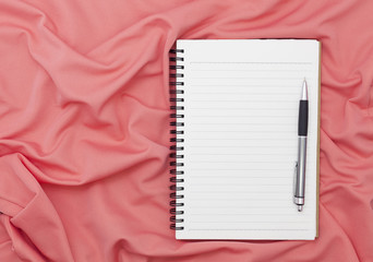Blank paper notebook with pen on beautiful pastel silk background.