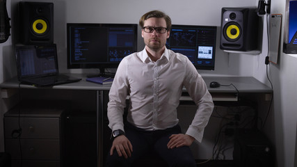 Poster - Portrait of white-collar worker dressed in white shirt and black trousers sitting on the chair. Skilled employee is prepairing for conference and waiting for his colleagues at his desk in the office.