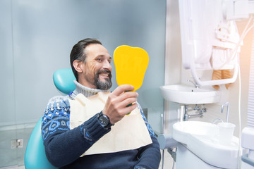 Man in a dental chair. Person smiling and holding mirror. Make your smile perfect.