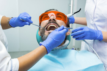 Two dentists with patient. Hands of doctors wearing gloves.