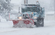 Snow plow with a red plow working in a blizzard