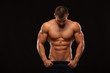 © satyrenko - Strong Athletic Man - Fitness Model showing Torso with six pack abs. stands straight and puts his hands in trousers. isolated on black background with copyspace