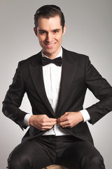 Poster - young elegant man unbuttoning his tuxedo while sitting