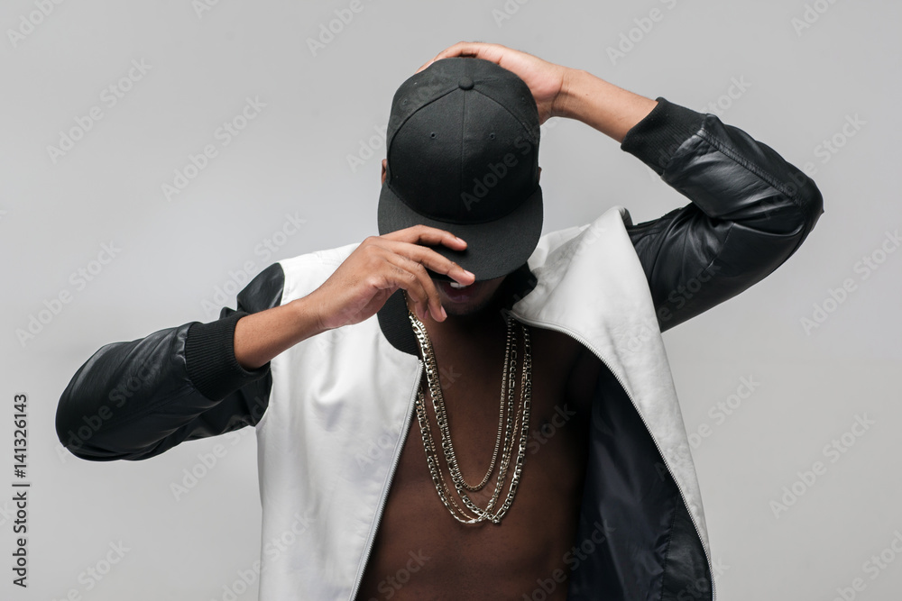 Black afroamerican rebellious rapper on grey background. Closed face, rejection, separated, reluctance to see, breaking off. Ghetto, challenge to society, cheeky, cool - obrazy, fototapety, plakaty 