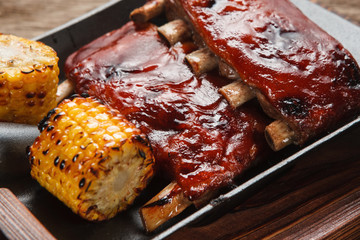 American delicious food. Appetizing grilled pork ribs with corn served on shovel, close up view. Junk food, picnic, bbq concept