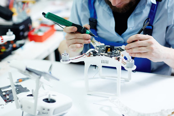 Closeup shot of unrecognizable man  testing electric current in circuit board of disassembled drone using multimeter tool on table in maintenance shop