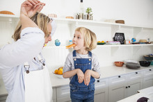 Mature Woman And Daughter Mimicking Rabbits With Carrots In Kitchen