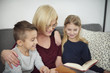 © Connect Images - Grandmother and grandchildren reading book on sofa