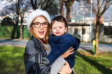 Portrait Of Young Woman In Santa Hat Carrying Baby Boy In Park