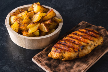 Grilled chicken breast on wooden board and grilled potato