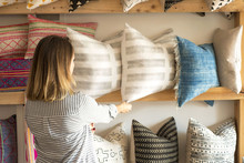Rear View Of Female Interior Designer Adjusting Cushions On Shelves In Retail Studio