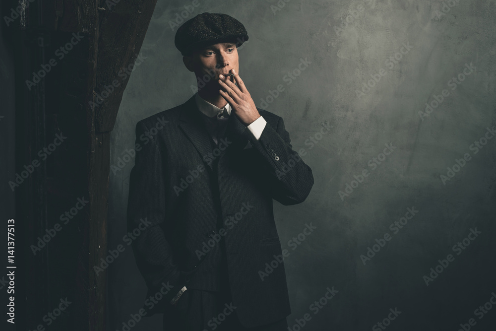 gangster smoking cigarette Retro 1920s english gangster smoking a cigarette. Wearing suit and flat  cap. Stock Photo